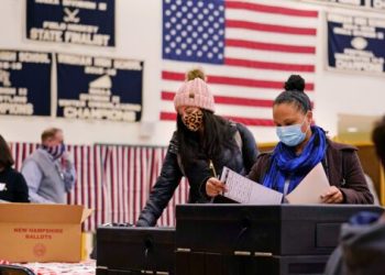 FILE - In this Nov. 3, 2020, file photo, two women, wearing protective masks due to the COVID-19 virus outbreak, cast their ballots at a polling station at Windham, N.H. High School. Regardless of the presidential election outcome, a vexing issue remains to be decided: Will the U.S. be able to tame a perilous pandemic that is surging as holidays, winter and other challenges approach? Public health experts fear the answer is no, at least in the short term, with potentially dire consequences. (AP Photo/Charles Krupa, File)